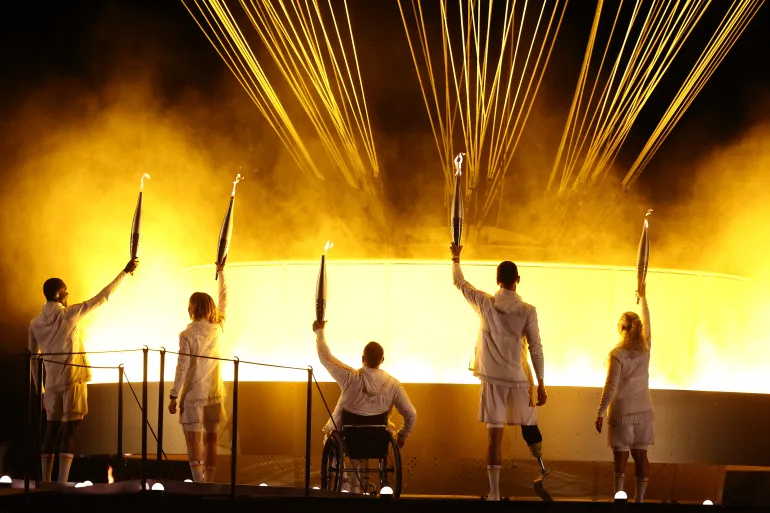 France’s Paralympic torchbearers hold the Paralympic flame in front of the Paralympic cauldron [Franck Fife/AFP]