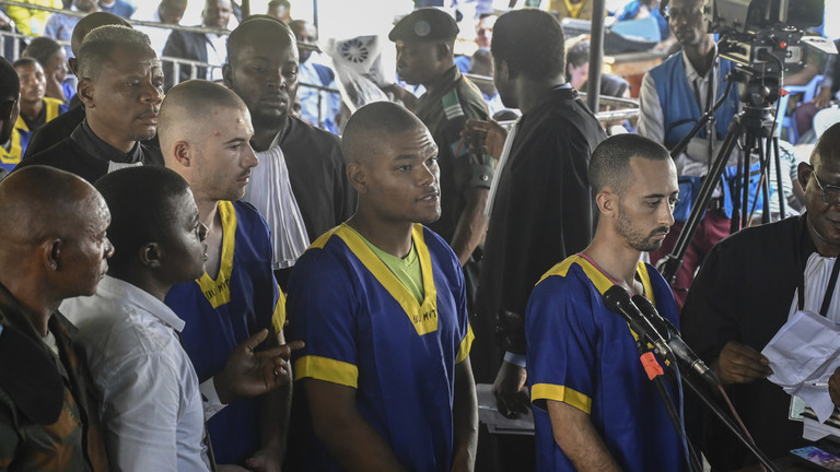 FILE PHOTO: Tyler Thompson Jr., Marcel Malanga and Benjamin Reuben Zalman-Polun, all American citizens, face the court in Kinshasa, Congo, with 52 other defendants, June 7, 2024, accused of a role in the attempted coup in Congo. © AP Photo / Samy Ntumba Shambuyi