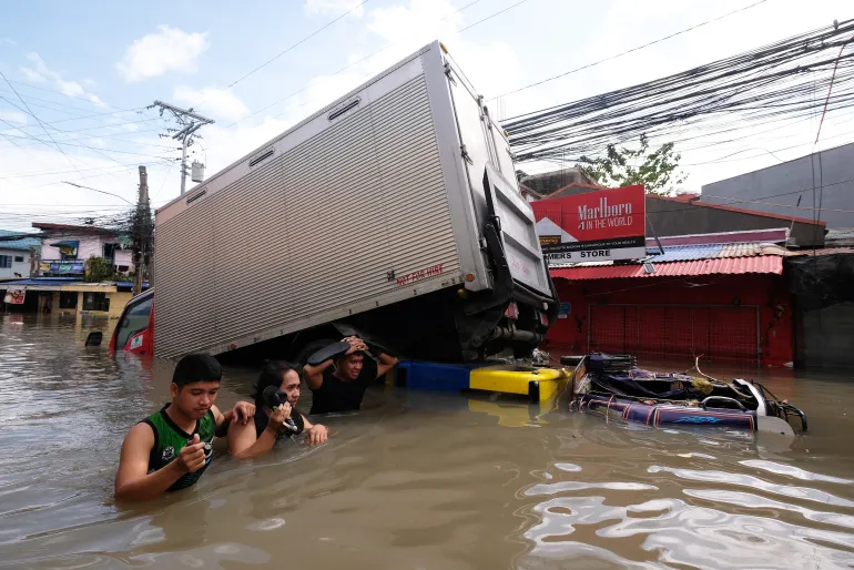 People wade through floods caused by Tropical Storm Trami in Naga in the Bicol region in central Philippines [Zalrian Sayat/AFP]