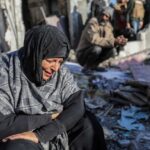 FILE PHOTO: A woman sits amongst damaged homes caused by Israeli air strikes, on January 18, 2024 in Rafah, Gaza. © Ahmad Hasaballah / Getty Images