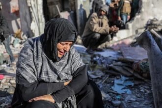 FILE PHOTO: A woman sits amongst damaged homes caused by Israeli air strikes, on January 18, 2024 in Rafah, Gaza. © Ahmad Hasaballah / Getty Images