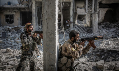 FILE PHOTO. Two armed soldiers of the Syrian Democratic Forces (SDF) standing next to a column of a destroyed building while battles against the Islamic State (IS) terror militia continue in Raqqa, Syria. © Morukc Umnaber/Getty Images