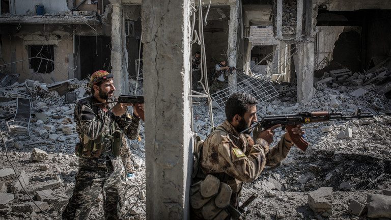 FILE PHOTO. Two armed soldiers of the Syrian Democratic Forces (SDF) standing next to a column of a destroyed building while battles against the Islamic State (IS) terror militia continue in Raqqa, Syria. © Morukc Umnaber/Getty Images