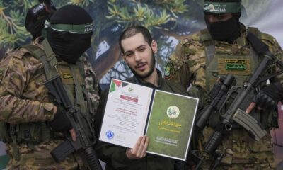 Israeli hostage Eliya Cohen, centre, is instructed to show a Hamas issued certificate while being escorted by militants to be handed over to the Red Cross in Nuseirat, central Gaza Strip, Saturday, Feb. 22, 2025. © AP Photo/Abdel Kareem Hana