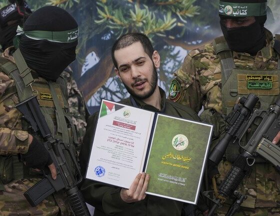 Israeli hostage Eliya Cohen, centre, is instructed to show a Hamas issued certificate while being escorted by militants to be handed over to the Red Cross in Nuseirat, central Gaza Strip, Saturday, Feb. 22, 2025. © AP Photo/Abdel Kareem Hana