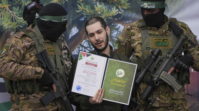 Israeli hostage Eliya Cohen, centre, is instructed to show a Hamas issued certificate while being escorted by militants to be handed over to the Red Cross in Nuseirat, central Gaza Strip, Saturday, Feb. 22, 2025. © AP Photo/Abdel Kareem Hana