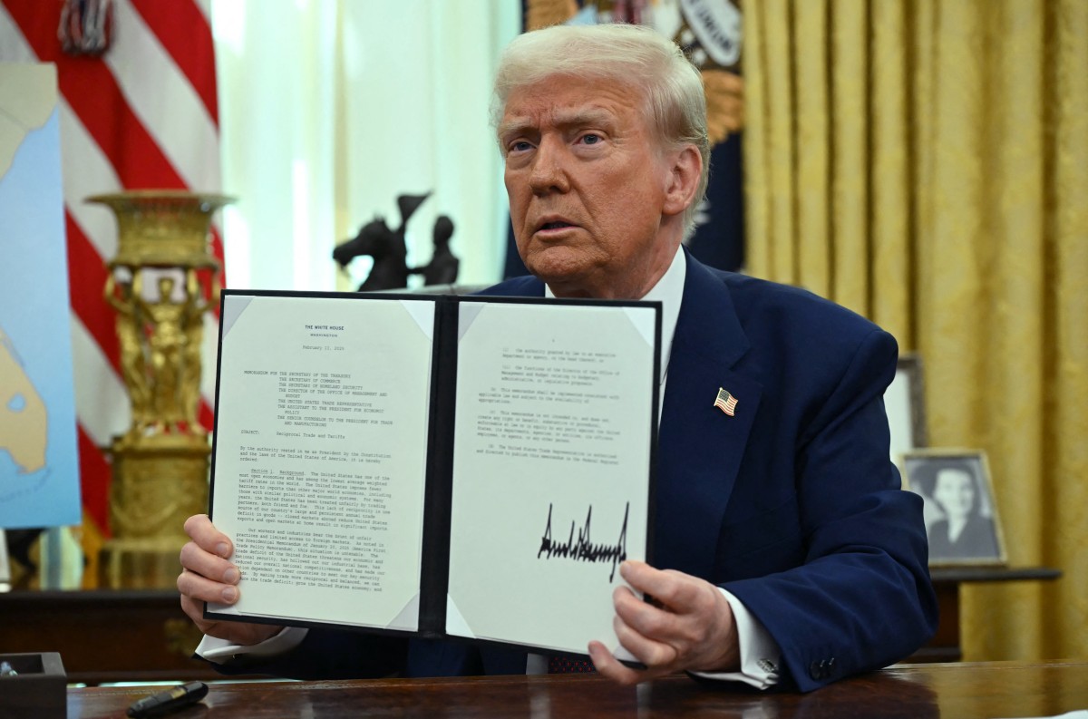 US President Donald Trump displays his signature on an Executive Order on reciprocal tariffs in the Oval Office of the White House in Washington, DC, on February 13, 2025. (Photo by ANDREW CABALLERO-REYNOLDS / AFP)